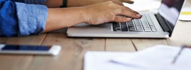 Person conducting business at a desk and typing on a laptop