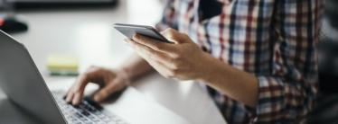 woman at laptop holding phone