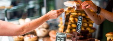 Woman behind bakery counter handing customer bag in exchange for money